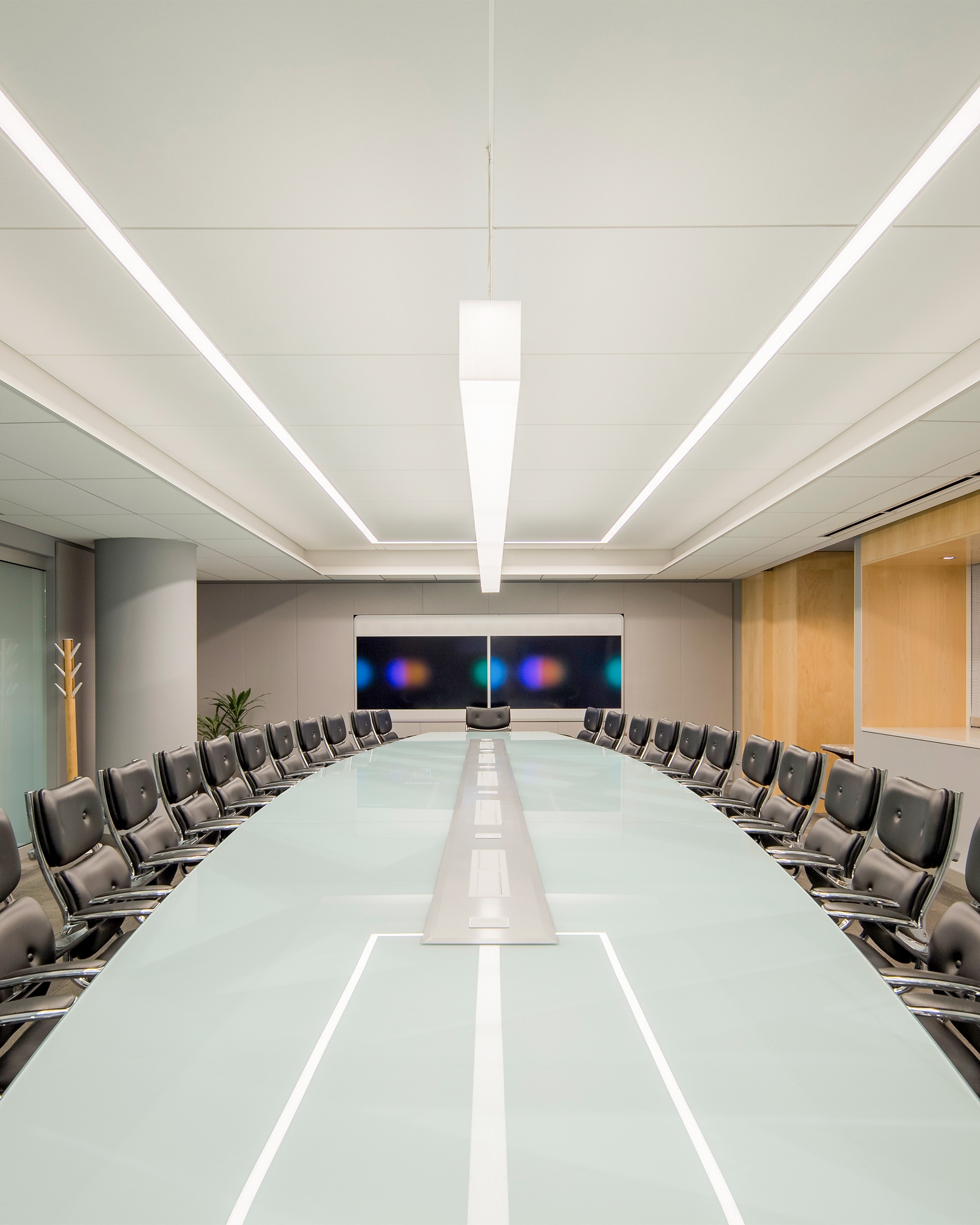 Jacob K. Javits Convention Center Executive Board Room. Refurbished existing conference table, modernized and customized with artwork underlay and glass top. Surrounding storefront system features switchable privacy glass. Custom ceiling design and lighting controlled by state-of-the-art Lutron Palladiom system.